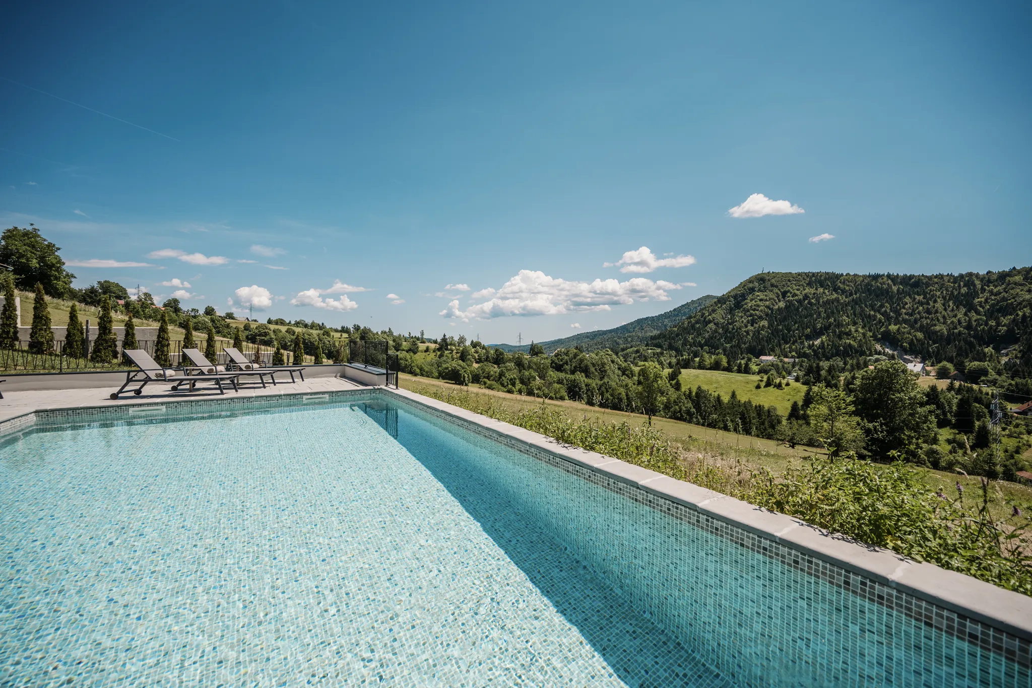 The 50 m2 heated pool and 40 m2 terrace opening straight into the Ravna Gora treeline in warm afternoon light