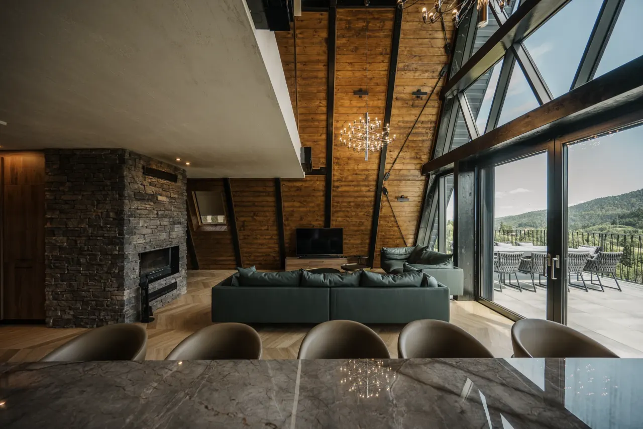 Double-height living room with a full triangular glass wall, starburst chandeliers and forest views