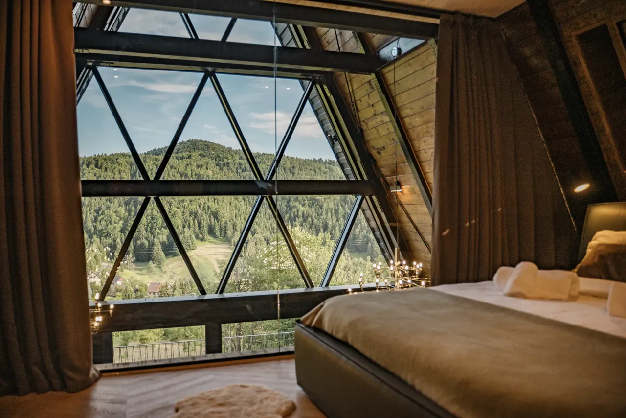 Top-floor bedroom framed by a gable glass wall opening onto the forest