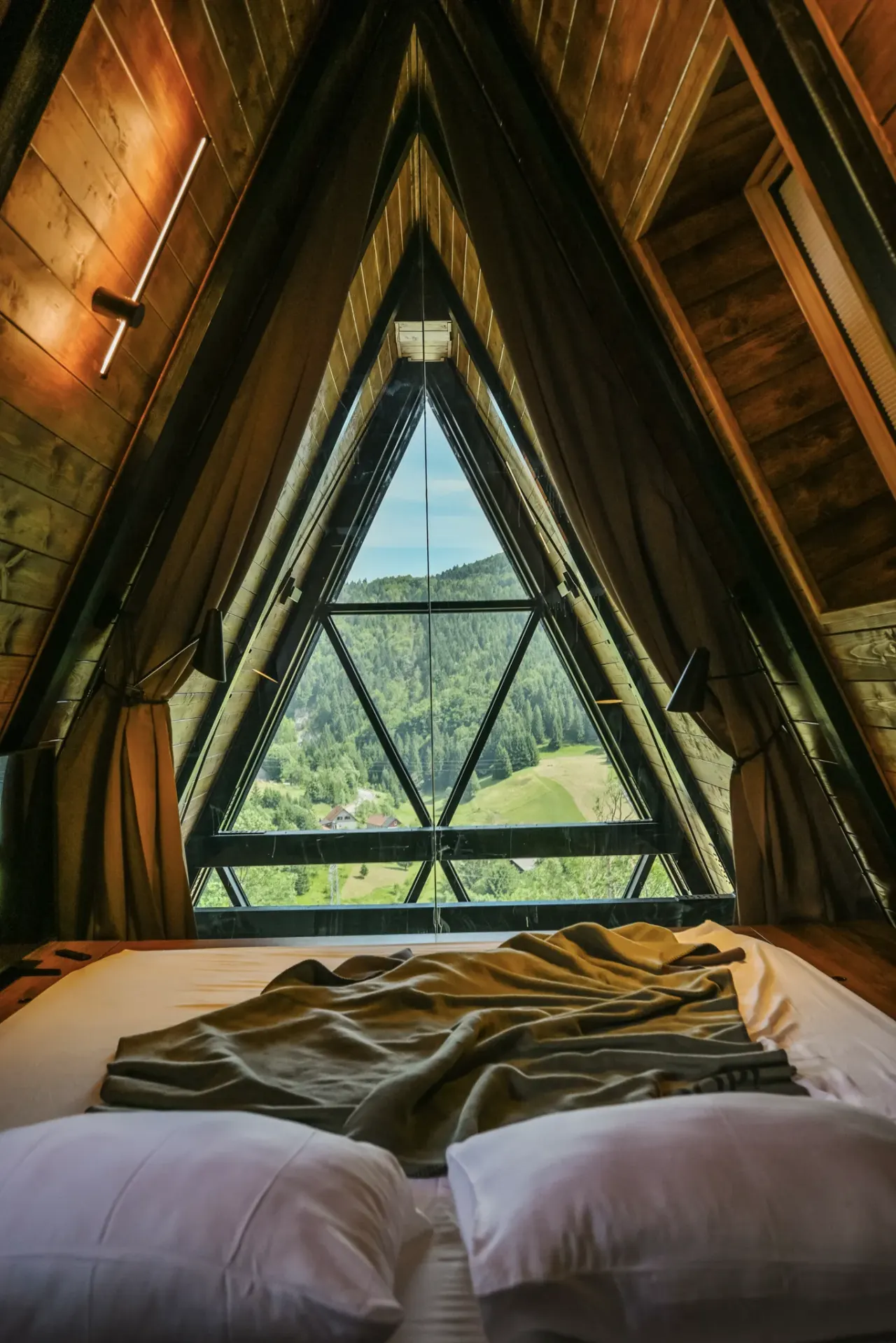 Spavaća soba uokvirena trokutastom staklenom stijenom A-frame krova