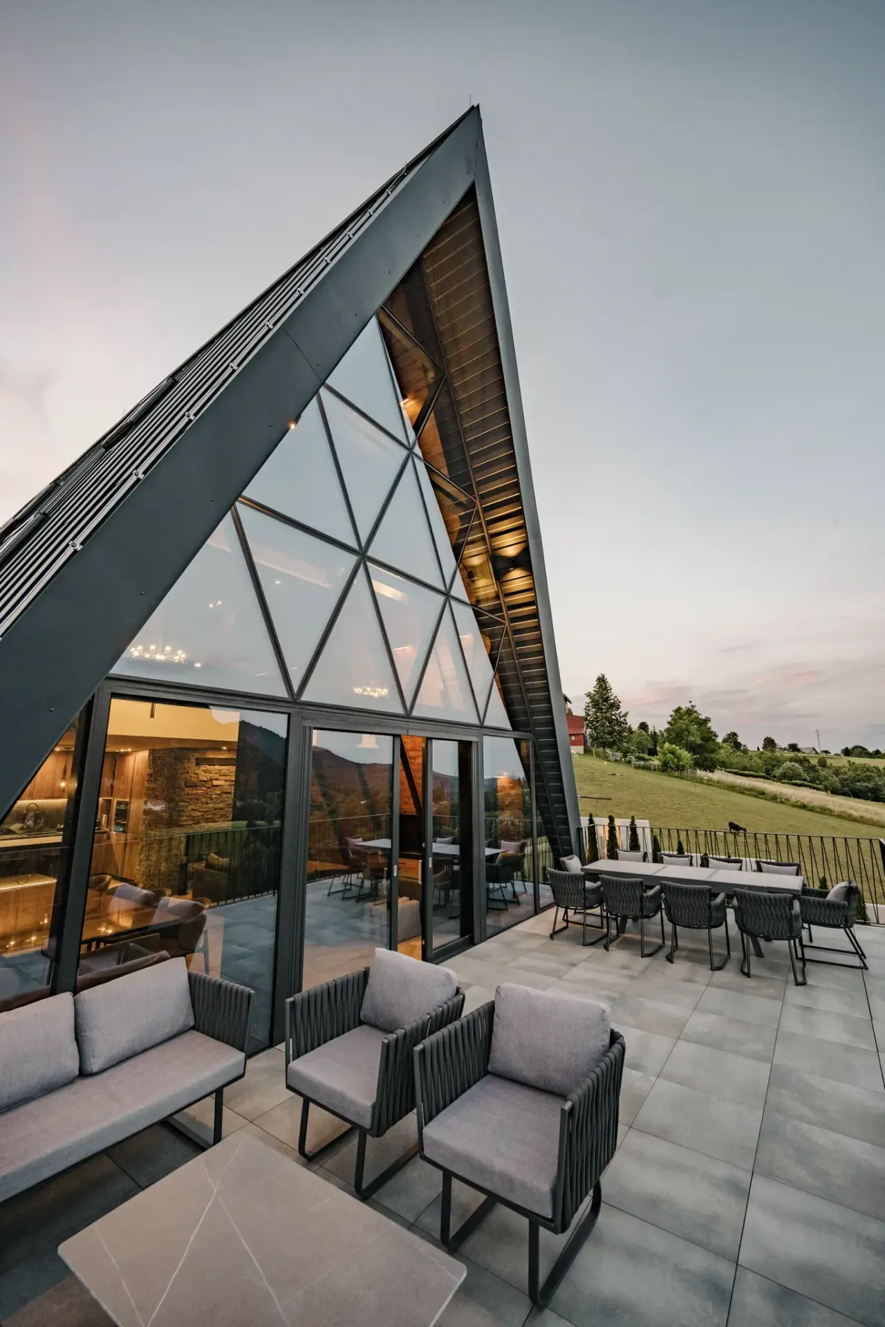 Osvijetljeni A-frame zabat iznad terase dok se večer spušta nad Gorski kotar